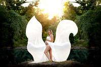 Pregnant mother to be in flown white dress standing on a rock in the middle of a stream in an NJ park.